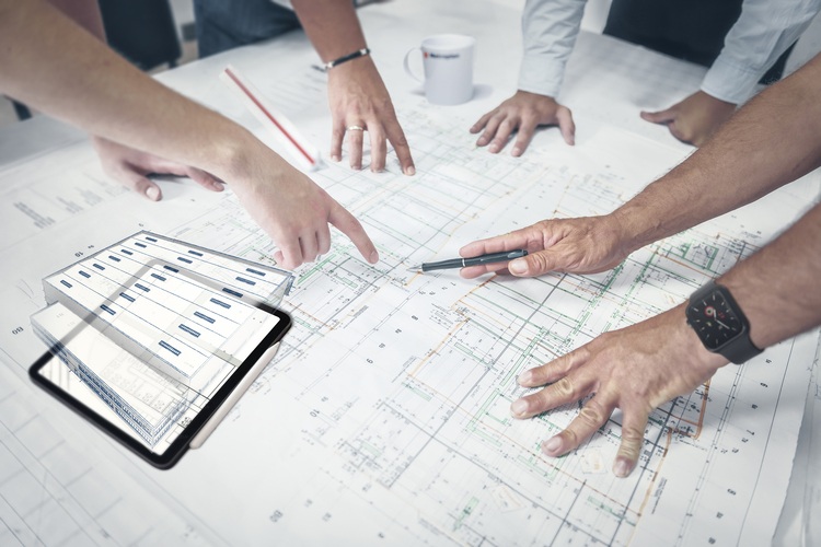 Team bei der Analyse von Bauplänen und Vertragsdokumenten, mit einem Tablet, das Vertrags- und Versicherungsdaten zeigt.