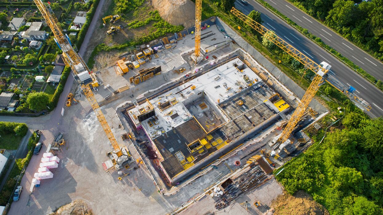 Luftaufnahme einer Baustelle mit mehreren Kränen und Grundstruktur eines Industriegebäudes – Beispiel für effiziente, nachhaltige Planung und Umsetzung eines Logistikbaus durch Generalplanung.