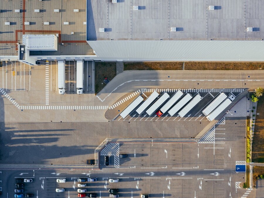 Luftaufnahme eines Logistikzentrums mit LKWs an der Laderampe – Symbol für optimierte Supply-Chain-Prozesse, Effizienz und Transparenz in der Logistik